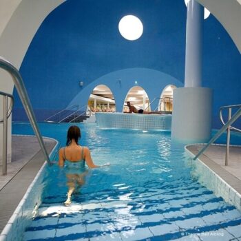 Weiblicher Badegast steigt die Treppen in das Indoorwasserbecken der Therme Bad Aibling