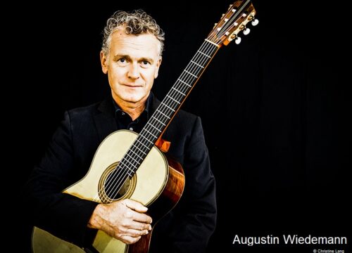 Augustin Wiedemann mit Gitarre im Arm vor schwarzem Hintergrund