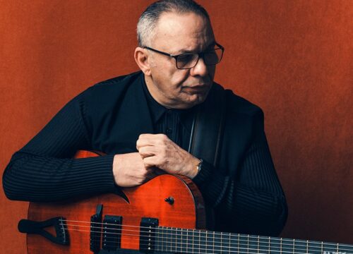 Bireli Lagrene mit Gitarre vor dunkelroter Wand