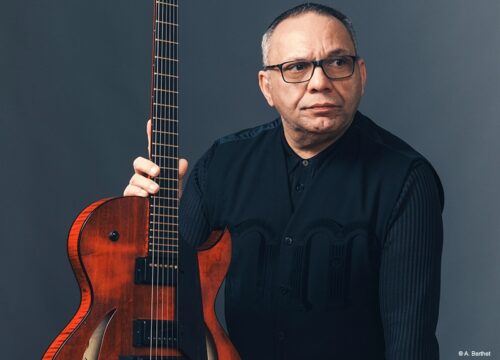 Bireli Lagrene hält Gitarre vor dunkelblauem Hintergrund