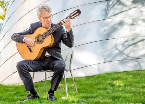 Eliot Fisk spielt in schwarzem Anzug draußen Gitarre