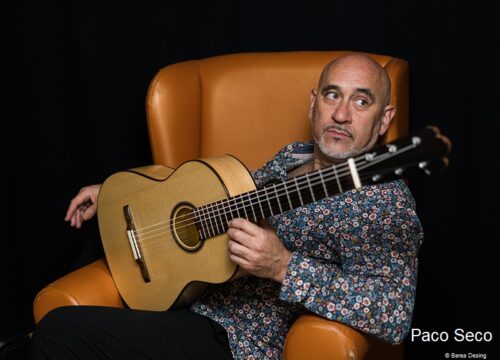 Paco-Seco-gallerie Paco Seco mit Gitarre auf Sessel vor schwarzem Hintergrund