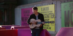 Daniel Stelter spielt Gitarre vor bunter Plakatwand