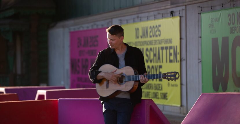 Daniel Stelter spielt Gitarre vor bunter Plakatwand