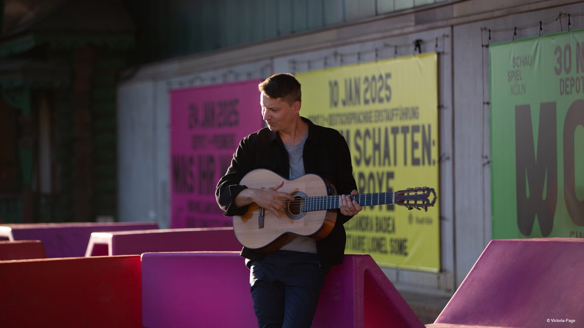 Daniel Stelter spielt Gitarre vor bunter Plakatwand