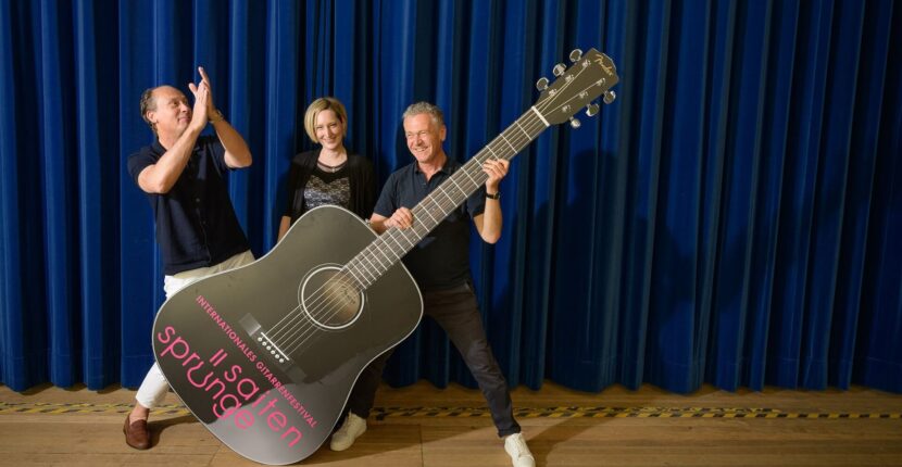 Das Festival-Team: Erkes, Stuber und Wiedemann mit großer Gitarre auf Bühne