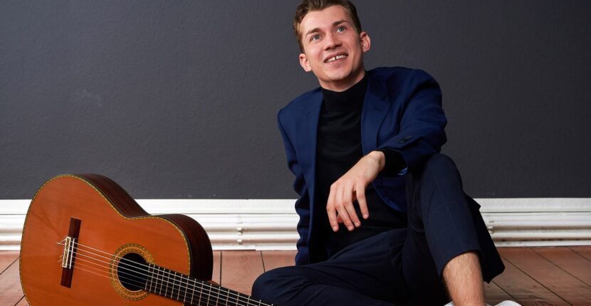 Gitarrist Thibaut Garcia sitzt auf Holzboden neben Gitarre