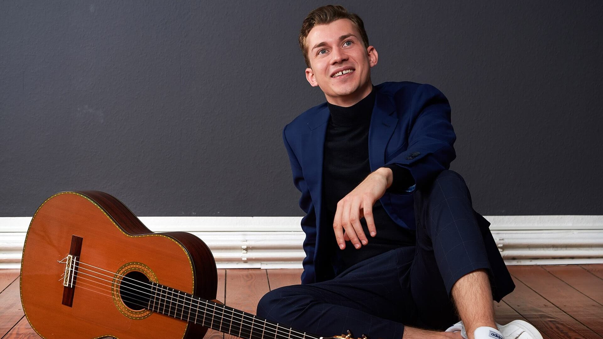 Gitarrist Thibaut Garcia sitzt auf Holzboden neben Gitarre